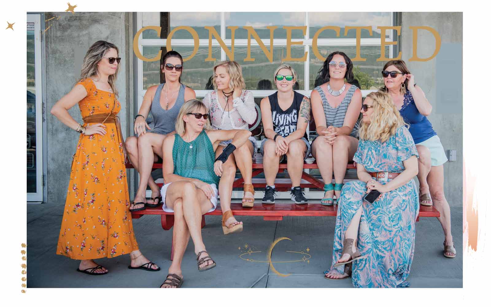 Eight women in boho attire posing for a photo on a red bench with a decorative border