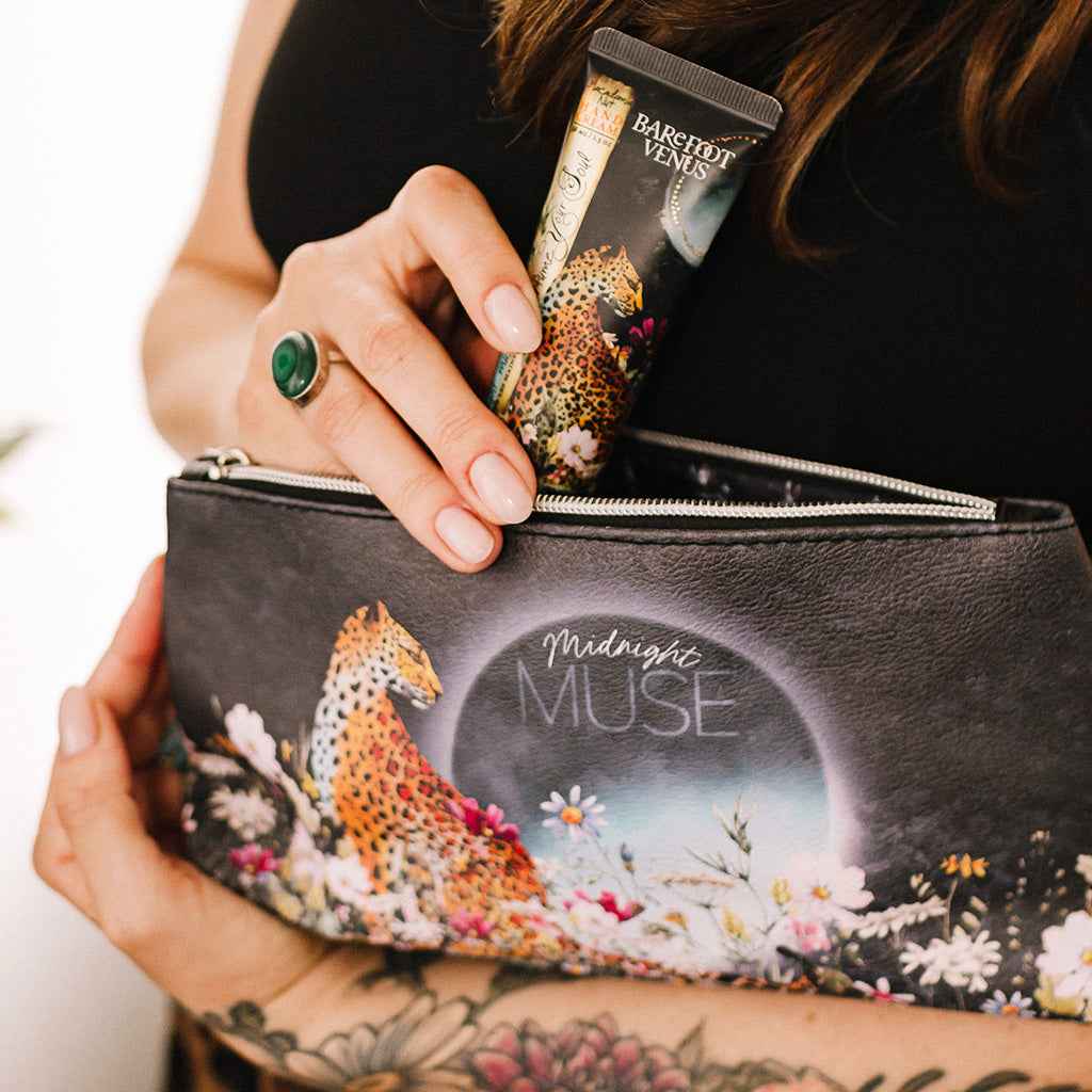 Person holding a vegan beauty bag with 'Midnight Muse' design, inserting Barefoot Venus hand cream.