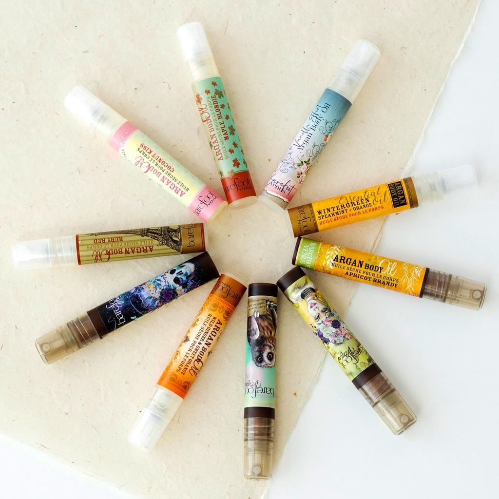 10 Barefoot Venus Mini Argan Oils displayed in a circle. Scents include Coconut Kiss, Maple Blondie, The Vanilla Effect, Wintergreen Spearmint, Lemon Freckle, Wild Ginger & Sweet Orange, Pink Pepper, Lavender Smoke, Ruby Red.