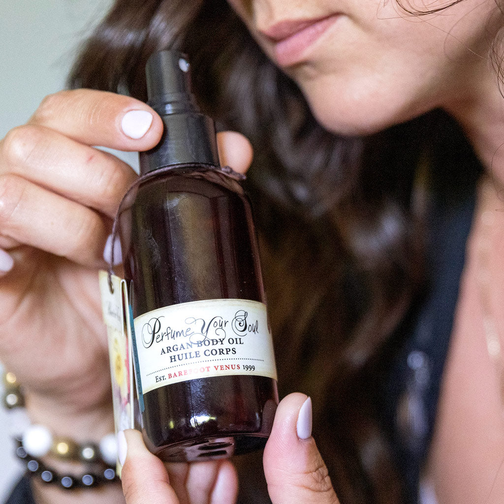 Person holding spray bottle of Barefoot Venus Black Coconut Argan body oil.
